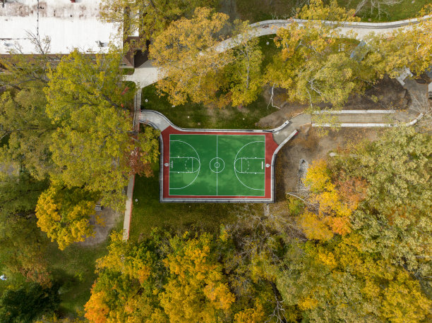 学校操场上绿色和红色的户外篮球场的航拍照片。场地包括挡土墙和黑色乙烯基涂层链环围栏。图片下载