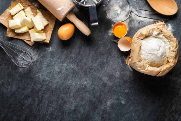 面包店的背景。烹饪材料烘焙面团，纸袋与面粉，鸡蛋，黄油，擀面棒和筛在黑暗的背景与复制空间顶视图图片下载