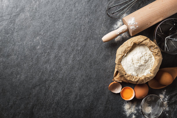 面包店的背景。烹饪材料烘焙面团，纸袋与面粉，鸡蛋，擀面棒和筛子在黑暗背景与复制空间顶视图图片下载