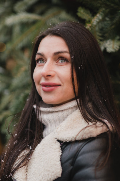 美丽的白人妇女穿着温暖舒适的衣服走在户外的圣诞集市上，雪花落在节日的灯光背景上。图片下载