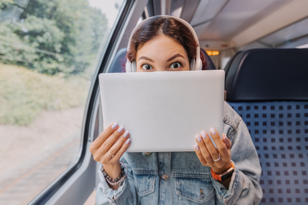 在火车旅行中，一个女孩藏在她的笔记本电脑后面，有一种有趣的情绪。个人数据盗窃、Wi-Fi网络和信息安全图片下载