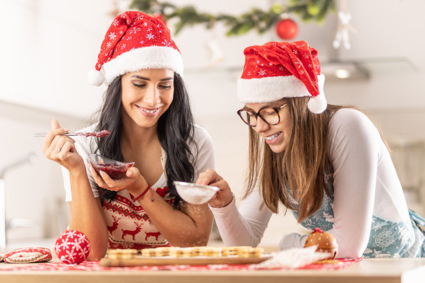 女儿帮妈妈做圣诞蛋糕，撒糖粉。图片下载