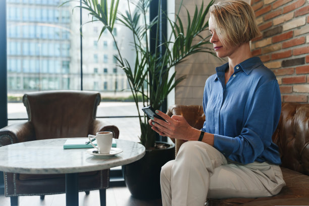 金发商务女性坐在咖啡馆用手机，喝着咖啡在办公室工作图片下载