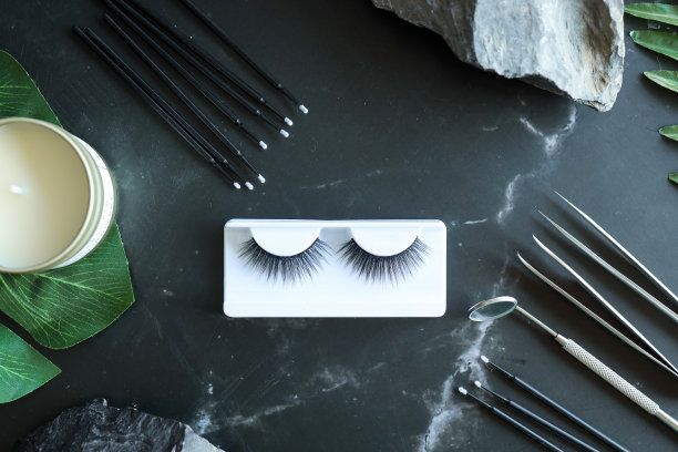 睫毛延伸工具在时髦的黑色背景和石头。假睫毛，镊子和刷子。美容沙龙。妆化妆品。俯视图，平铺图片下载