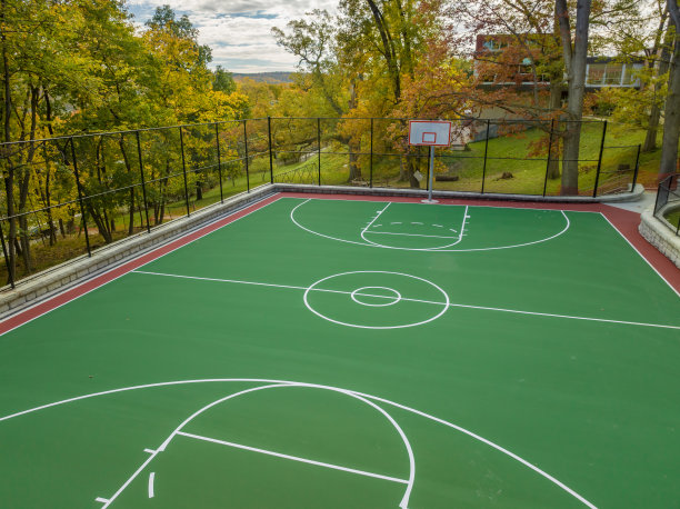 学校操场上绿色和红色的户外篮球场的航拍照片。场地包括挡土墙和黑色乙烯基涂层链环围栏。图片下载