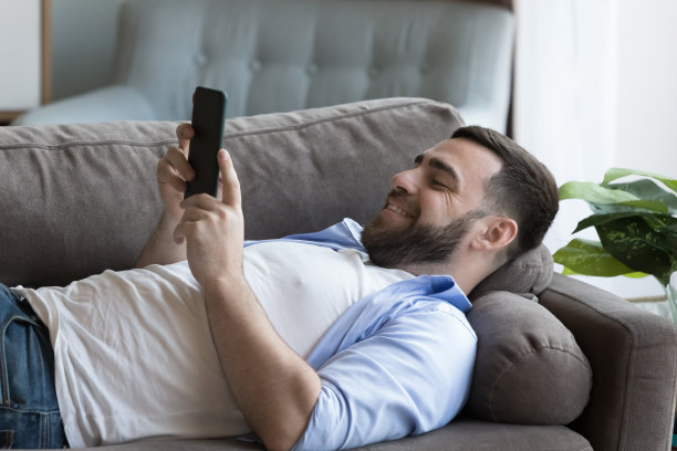 单身男子躺在沙发上，拿着智能手机图片下载