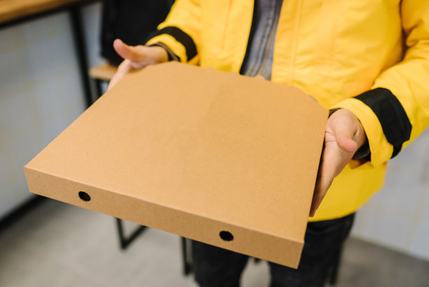 拿着纸板披萨盒的快递员。棕色盒子，用于运输和送货。订餐服务和外卖理念。从顾客家里订购快餐。放置文字和广告的地方。图片下载