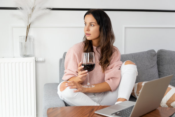 女人坐在沙发上，端着一杯红酒图片下载