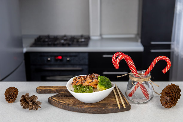 厨房的桌子上放着一盘金色的米饭、大虾、青豆和西兰花。桌上放着一罐新年糖果和松果。亚洲食物和圣诞概念图片下载