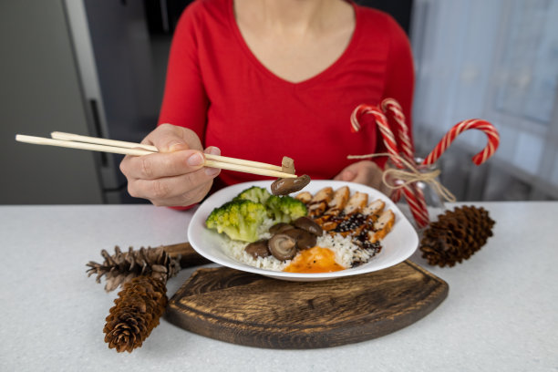 一个穿着红色衬衫和棕色围裙的女孩手里拿着一盘金色的米饭、鸡肉、西兰花、香菇和unagi酱。这道菜用芝麻装饰。亚洲食物概念图片下载