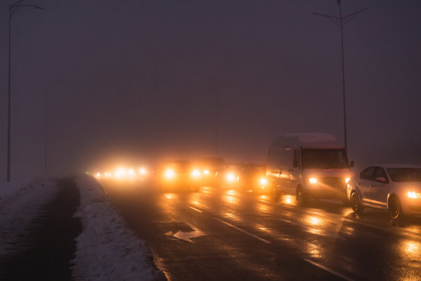 多雾的天气。夜雾。路面能见度低。汽车的运动。交通堵塞。湿滑的沥青。汽车头灯。一缕光。路上有冰雪。城市街道图片下载