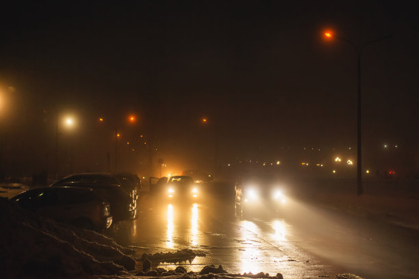 多雾的天气。夜雾。路面能见度低。汽车的运动。交通堵塞。湿滑的沥青。汽车头灯。一缕光。路上有冰雪。城市街道图片下载