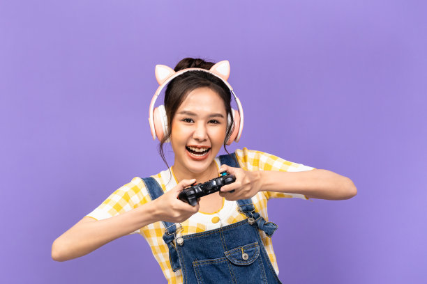 美丽的亚洲年轻女子在休闲的黄色t恤和玩电子游戏使用操纵杆与紫罗兰色的背景隔离。图片下载