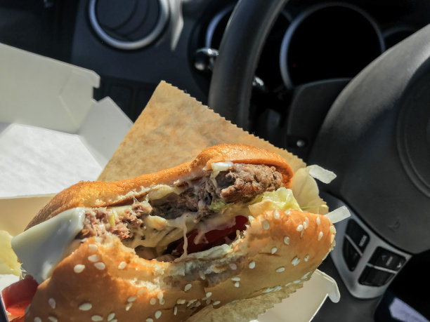 边开车边吃:在车里手里拿着一个咬过的汉堡。方向盘背景图片下载