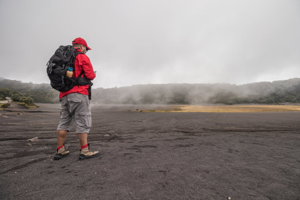 在伊拉苏火山国家公园，游客背着背包和防水夹克，在植被和雾的包围下查看手机图片下载