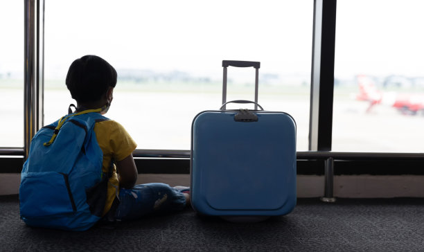 在机场候机楼，带着行李箱的孩子望着窗外。孩子和行李箱在机场，在室内，等待去旅行。图片下载