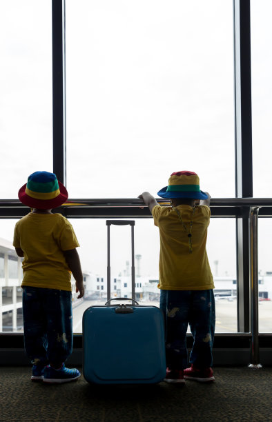 在机场候机楼，带着行李箱的孩子望着窗外。孩子和行李箱在机场，在室内，等待去旅行。图片下载