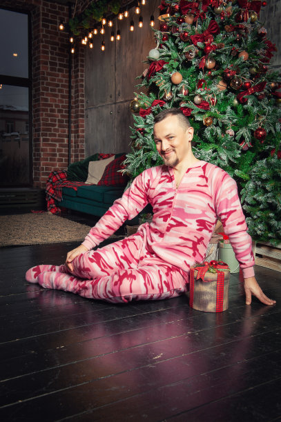 快乐有趣的人穿着睡衣坐在地板上，靠近装饰杉树和拿着圣诞礼物图片下载