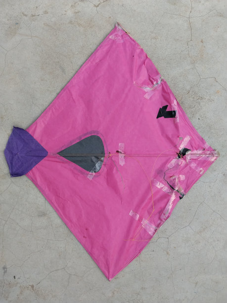 表面是粉色和黑色的风筝，周围用胶带修补了很多次。破风筝掉在地上图片下载