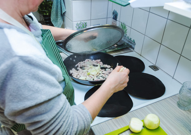 一位年轻的白人妇女在煎锅里煎肉和蔬菜。一位妇女在家里的厨房里准备食物。图片下载
