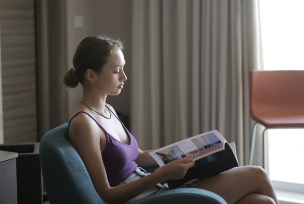 一位年轻的女性坐在扶手椅上，在房子的灯光下看杂志图片下载