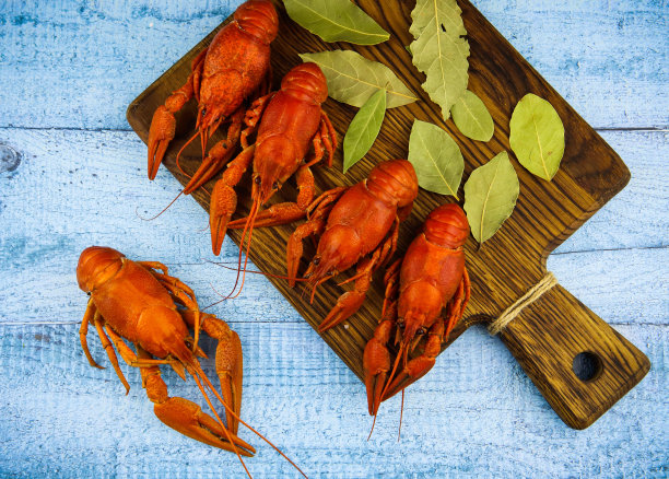 用香草和一片柠檬煮小龙虾放在砧板上。蓝色木制背景。图片下载