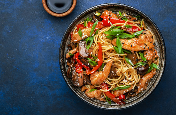 将面条与鸡肉、红辣椒、香菇、香葱和芝麻放入碗中翻炒。亚洲菜。蓝色桌面背景，俯视图图片下载