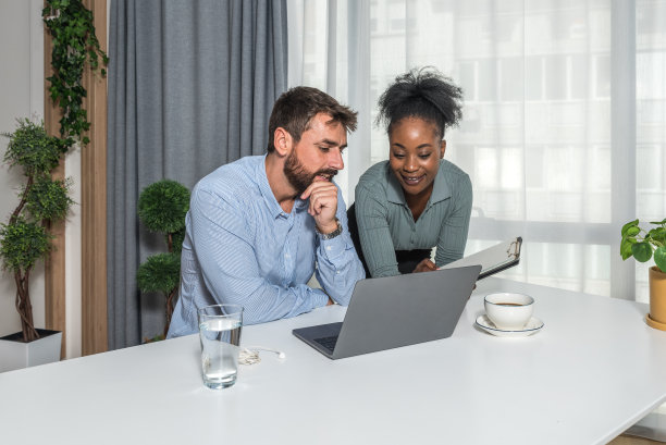 两个业务伙伴在办公室工作，在日历年底用笔记本电脑查看和阅读统计数据。商人、小公司老板使用电脑进行网上贸易。图片下载