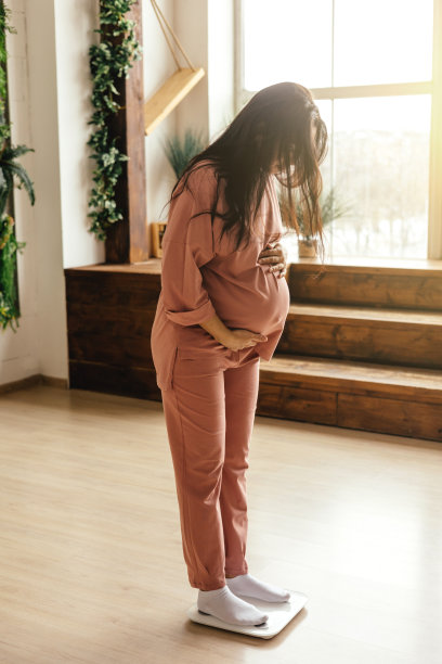 一个怀孕的女孩在测量她的体重并看着秤图片下载