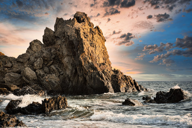 海滩上的日落，有一块大石头和海浪。图片下载