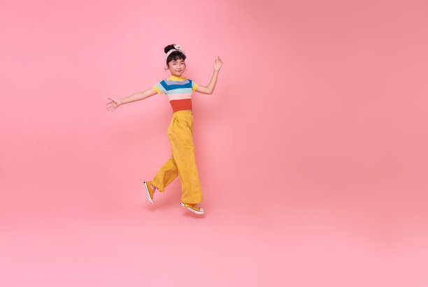 快乐的亚洲女孩跳到空白旁边孤立的粉红色背景。图片下载