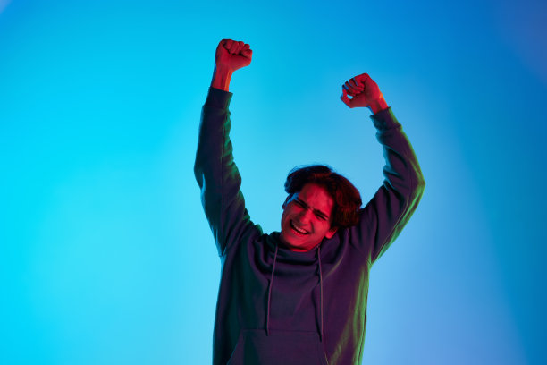 肖像的年轻男子卷发摆姿势与获胜的表情孤立的蓝色背景在霓虹灯图片下载