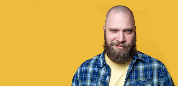 特写肖像胡子野蛮微笑的人看着相机在黄色的背景。模拟，模板，复制空间。自信、英俊、严肃。休闲装，格纹蓝衬衫和牛仔裤。图片下载