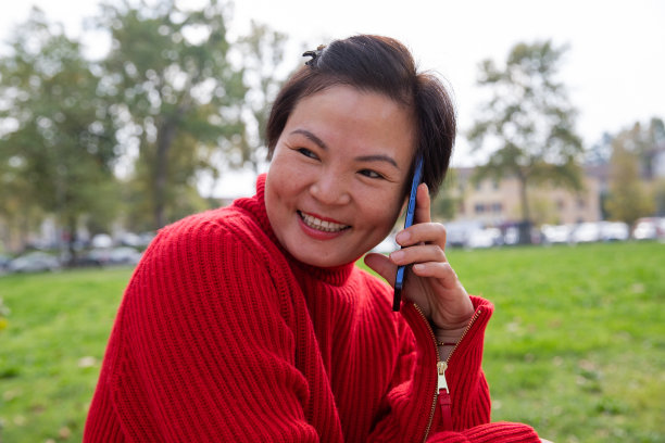 在公园用手机交谈的笑容灿烂的中国女人图片下载