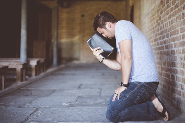 一个男人跪在地上，用圣经抵着他的头祈祷的特写镜头图片下载