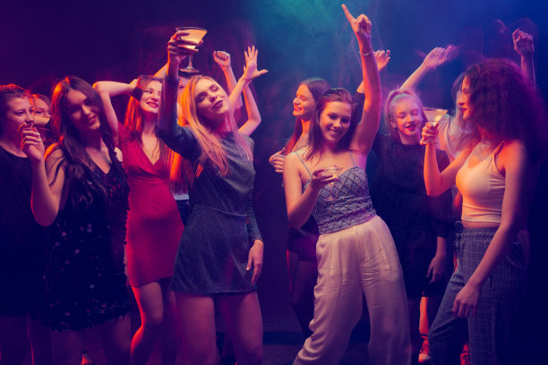一群年轻人，美丽的女孩参加派对，跳舞，在霓虹灯的黑暗背景下玩得很开心图片下载