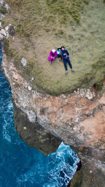 垂直鸟瞰图，一对情侣坐在巴厘岛的绿色悬崖上，浪花飞溅图片下载