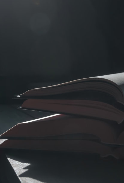 木桌上放着一叠打开的书。打开的书一摞一摞地放着。在一个黑暗的房间里，打开的书被从窗户射进来的光扫过——这是一张垂直的照片。图片下载