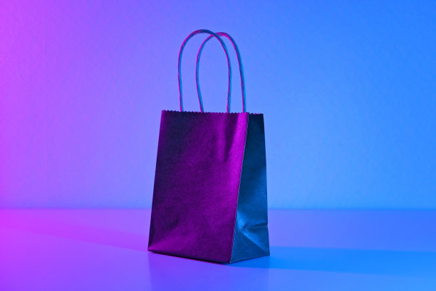 霓虹灯下的黑色纸袋。蓝色粉色背景下的促销、黑色星期五、网络星期一的概念。极简主义。礼物，购物，购物。图片下载