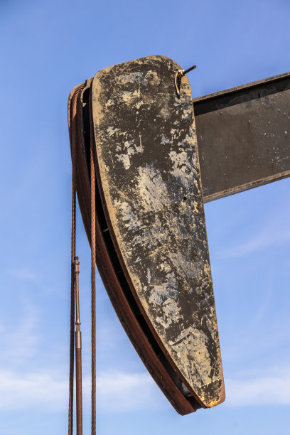 湛蓝的天空映衬着锈迹斑斑、肮脏不堪的油井马头，上面有缰绳或电缆图片下载
