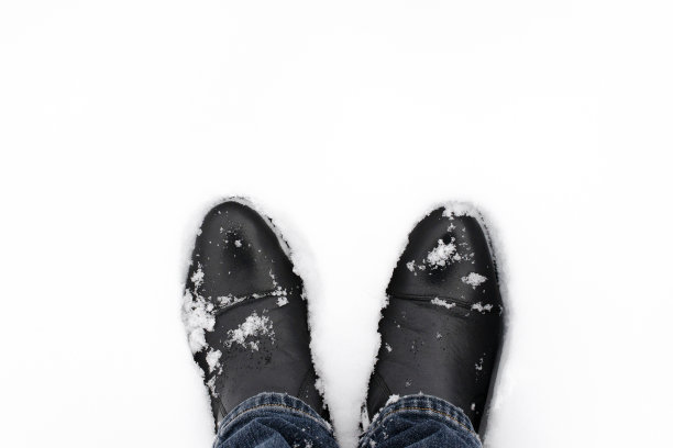 冬天的季节。新雪中鞋子的俯视图。雪地里穿着黑色靴子和蓝色牛仔裤的腿，俯视图。刚下过雪的靴子道俯视图。图片下载