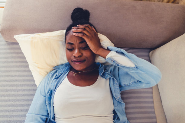 一名年轻女子在家中遭受胃痉挛的镜头。一名年轻女子胃痉挛的照片。有腹部问题的妇女在床上，她用手按摩疼痛的地方。图片下载