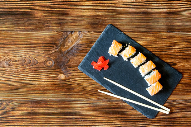 鱼寿司卷与三文鱼，山葵和筷子在黑色砧板上木制的乡村背景与复制空间。海鲜，餐厅概念的餐饮服务，平铺图片下载