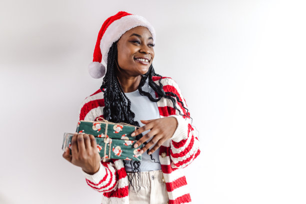 戴着圣诞帽的年轻女子拿着圣诞礼物站在白墙前图片下载