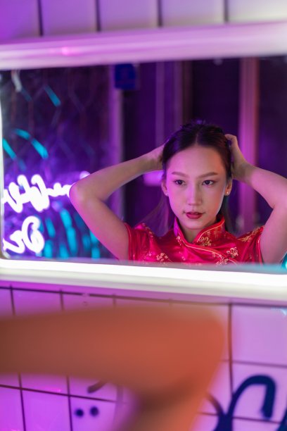 工作室肖像照片的一个美丽的年轻的亚洲女性模特穿着优雅的红色传统中国服装旗袍服装站在镜子玻璃前准备她的头发图片下载