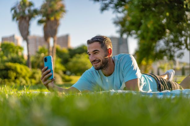 一个西班牙人躺在城市公园的毯子上看他的手机。图片下载