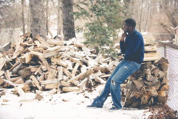 男性穿着蓝色运动衫，坐在被砍断的树干上思考图片下载