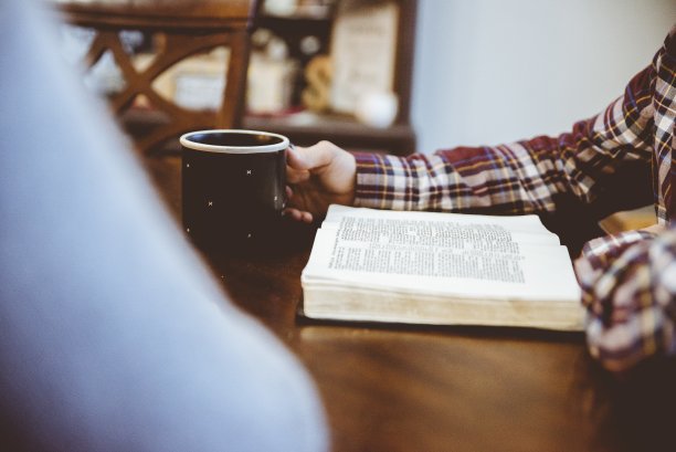 一个男人边喝咖啡边看书的特写镜头和模糊的背景图片下载