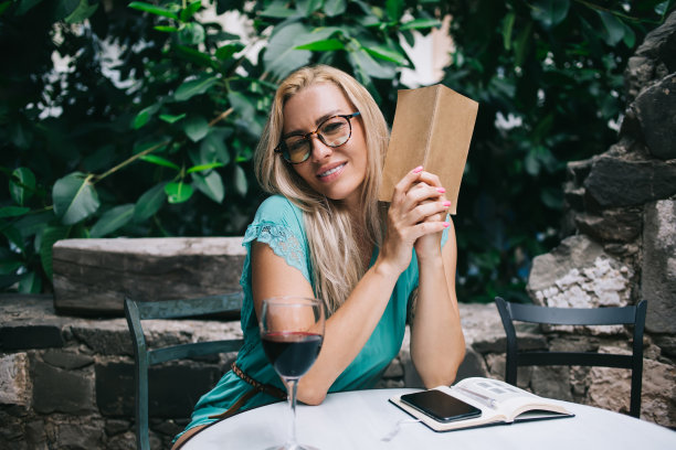 画像微笑的白人诗人看着相机，分析文学教科书坐在街头桌子与酒杯，迷人的年轻女子与书享受休闲阅读图片下载