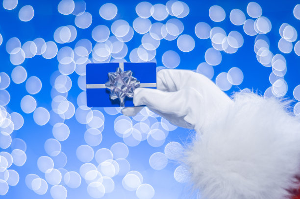 圣诞老人的手拿着蓝色的礼物卡在蓝色的背景和白色的散焦图片下载